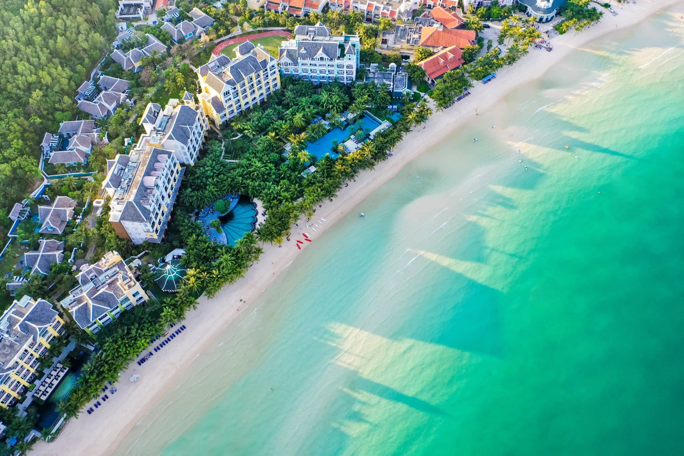 A beachfront resort on Bãi Kem, Phú Quốc, seen from above with swimmers in the turquoise shallows